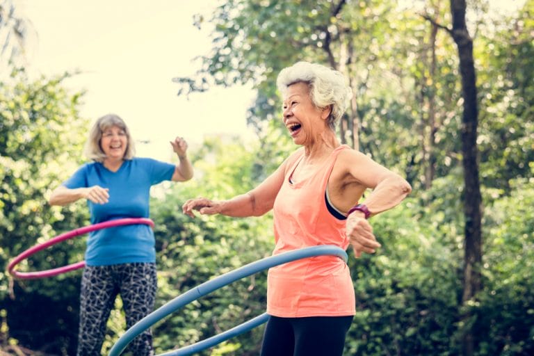 Two seniors with high blood pressure play with hula hoops in the park.