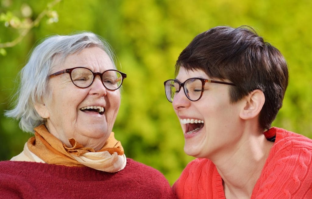 Two elderly women enjoying each other's company in a park while receiving home care services.