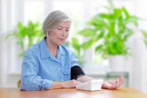 A woman is monitoring her blood pressure levels with an electronic device, focusing on high blood pressure in seniors.