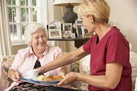 A nurse serving food to an elderly woman in a living room.
