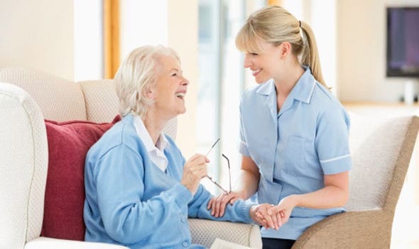A woman talking to an elderly woman in a nursing home.