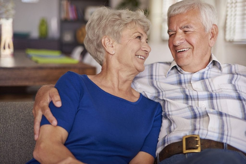 An older couple having a fluff on a couch and tuck moment, laughing.