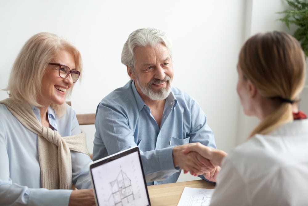 Two elderly people shaking hands at a meeting with a realtor to discuss property resources.