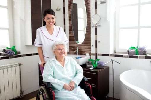 A nurse in a wheelchair with an elderly woman in a bathroom.