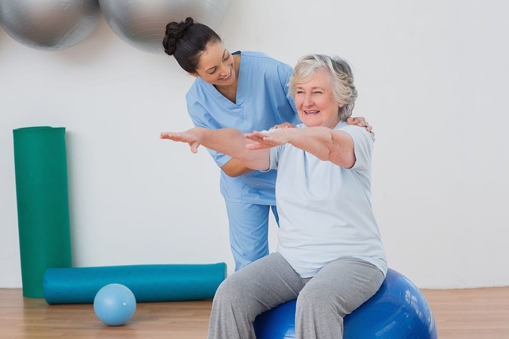 A physical therapist guides an elderly woman through safe exercises on an exercise ball.