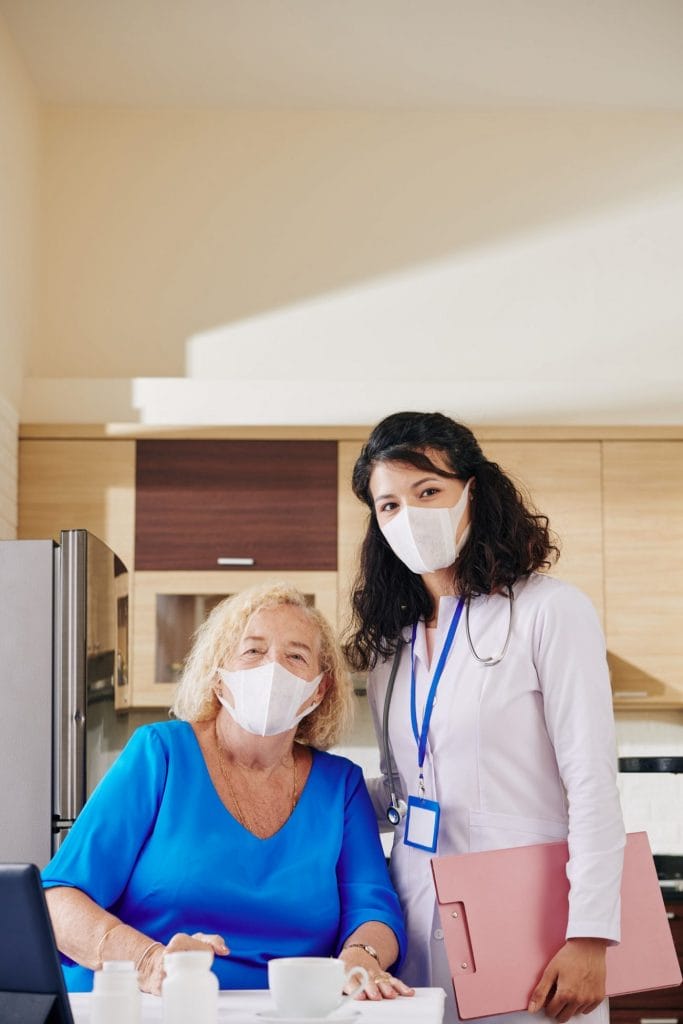 A woman wearing a face mask and an older woman in a kitchen.