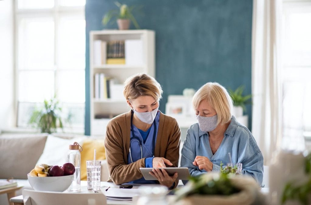 Two women in surgical masks using a tablet at home.