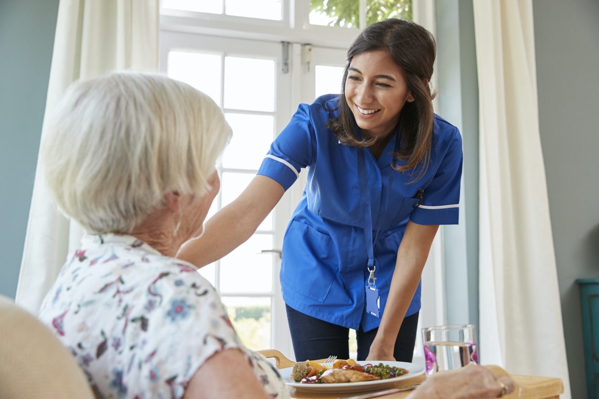 A nurse serving a meal to an elderly woman.