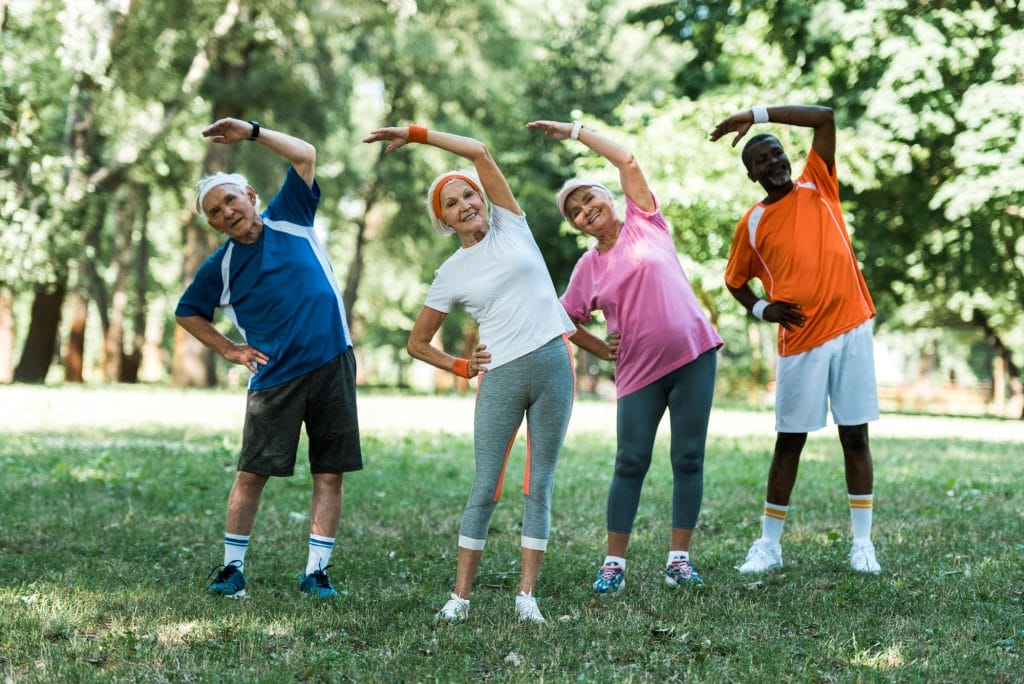 cheerful multicultural retired men and women standing with hands on hips while doing stretching