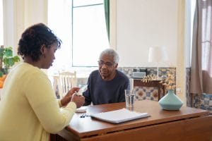 A caregiver is conversing with an elderly gentleman over a meal.