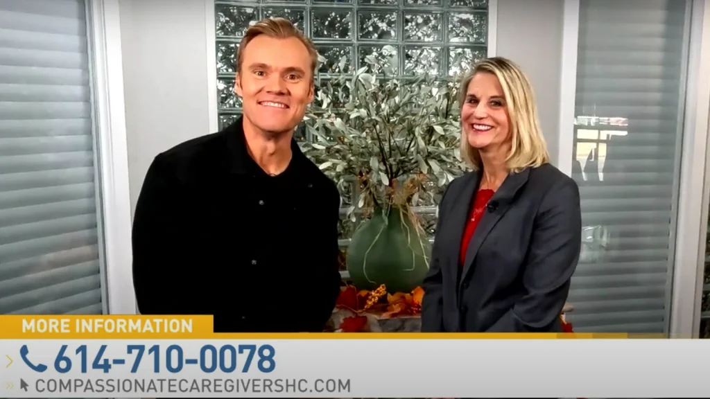 Two people smiling indoors next to a vase with leafy branches, capturing the essence of warmth and comfort that Home Care Columbus provides. Contact information is displayed at the bottom.