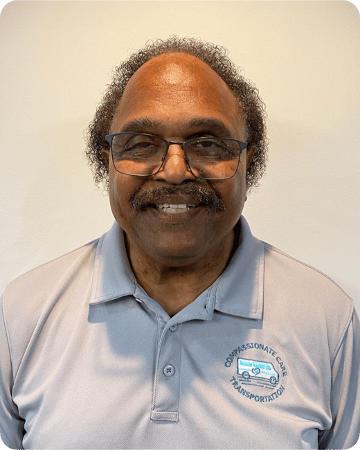 Smiling man wearing glasses and a blue polo shirt with a "Compassionate Care Transportation" logo.