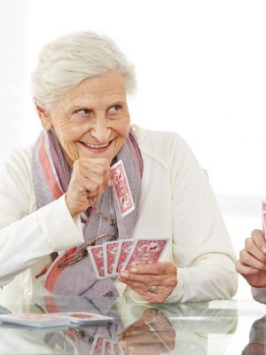 Two elderly women engaged in an enjoyable game of cards within the comfort of their own home, emphasizing a need for in-home care.