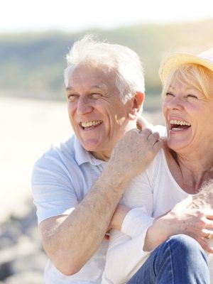 An older couple is smiling while enjoying home care on the beach.