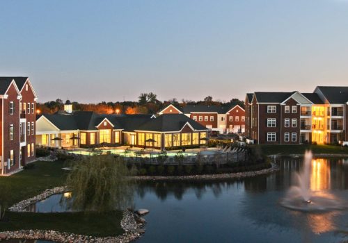 An apartment complex with a pond and fountain at dusk.