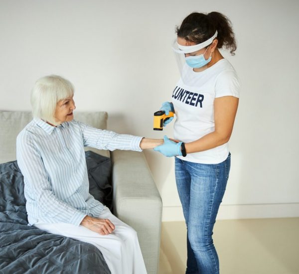 A woman wearing a mask and gloves is helping an elderly woman.