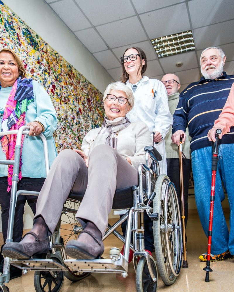 A group of elderly people in wheelchairs walking down a hallway.